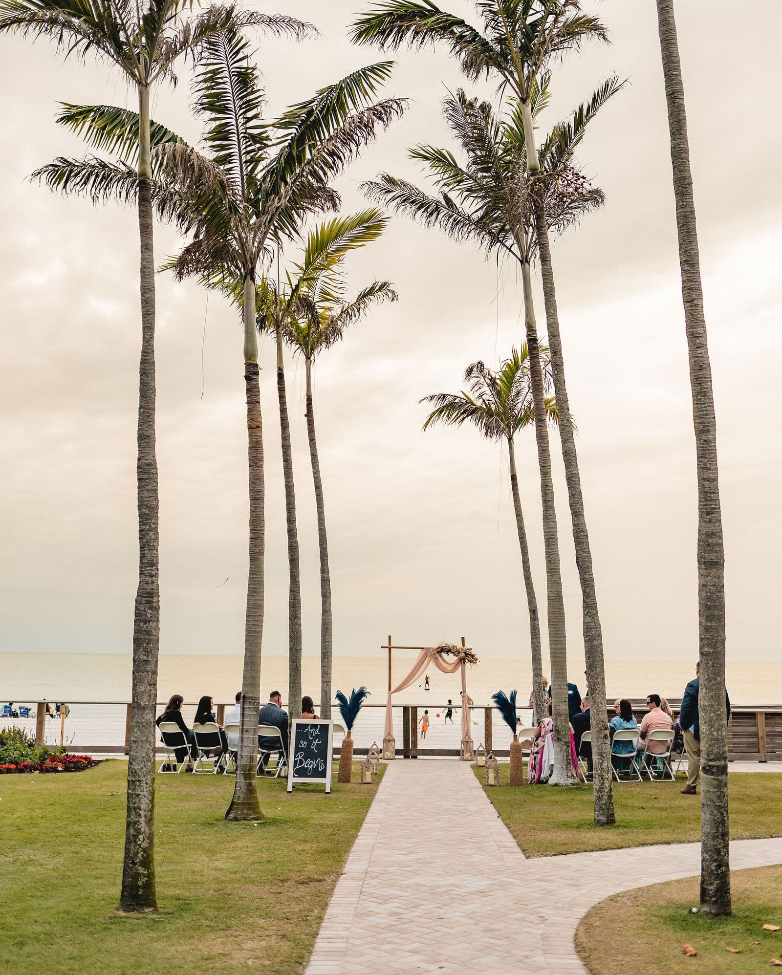 Landscaped beach-access walkway to 8th Ave S Wedding Beach in Naples, Florida, with a wedding arch set up on the sand near the Gulf of Mexico