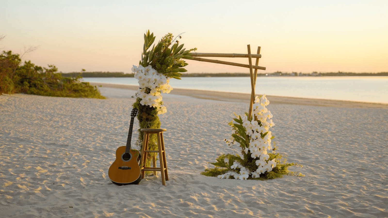 Illustrative acoustic guitar beside a beach ceremony arch at sunset