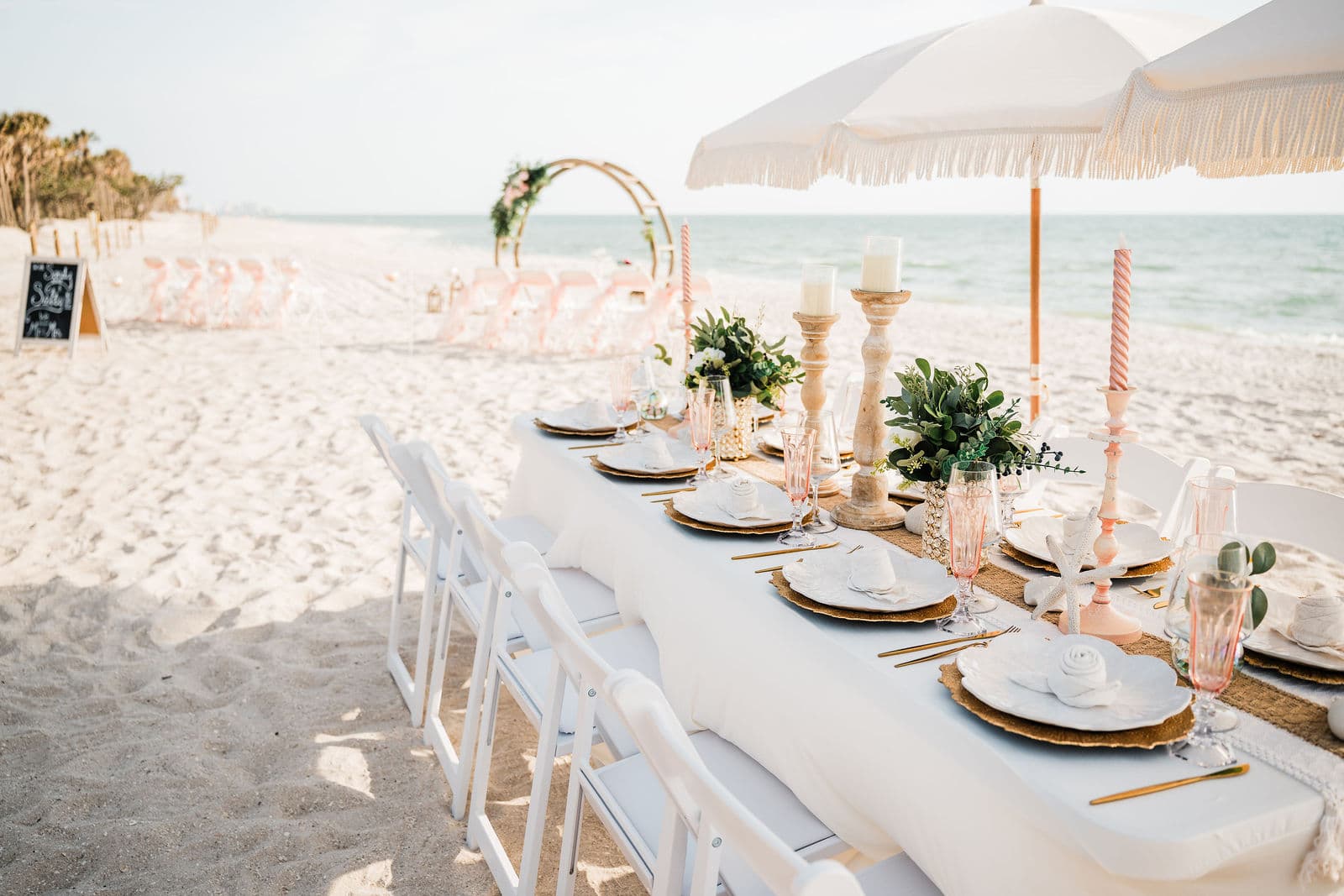 Elegant beach wedding ceremony setup on Navarre Beach Florida with white chairs facing a floral arch and emerald Gulf water in the background