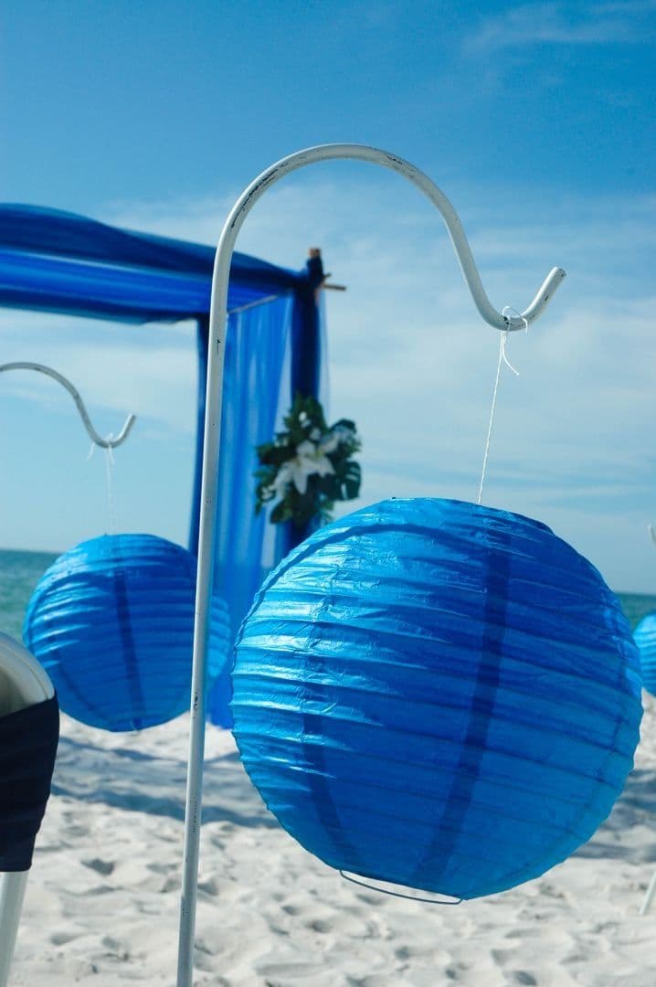 Blue paper lanterns hanging on a beach with a blue draped backdrop.
