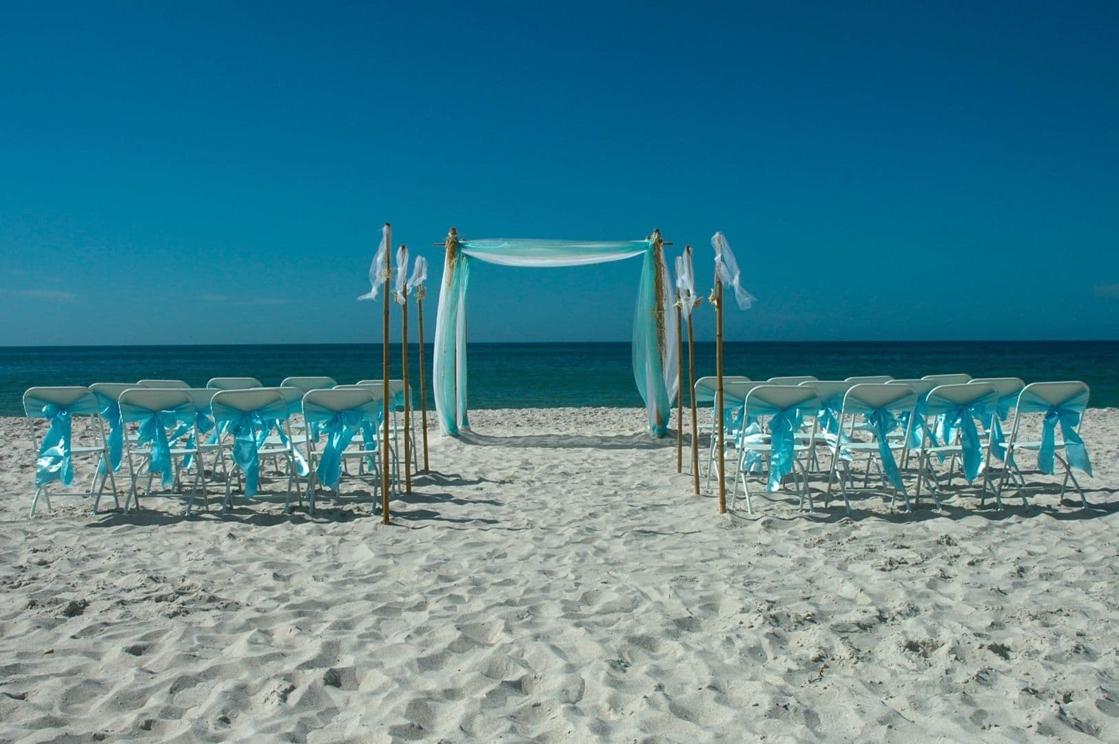 Beach wedding setup with chairs, arch, and blue accents.