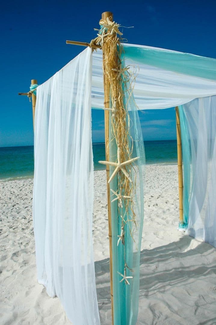 Beach wedding canopy with white and turquoise fabric, starfish decor, and blue sky.