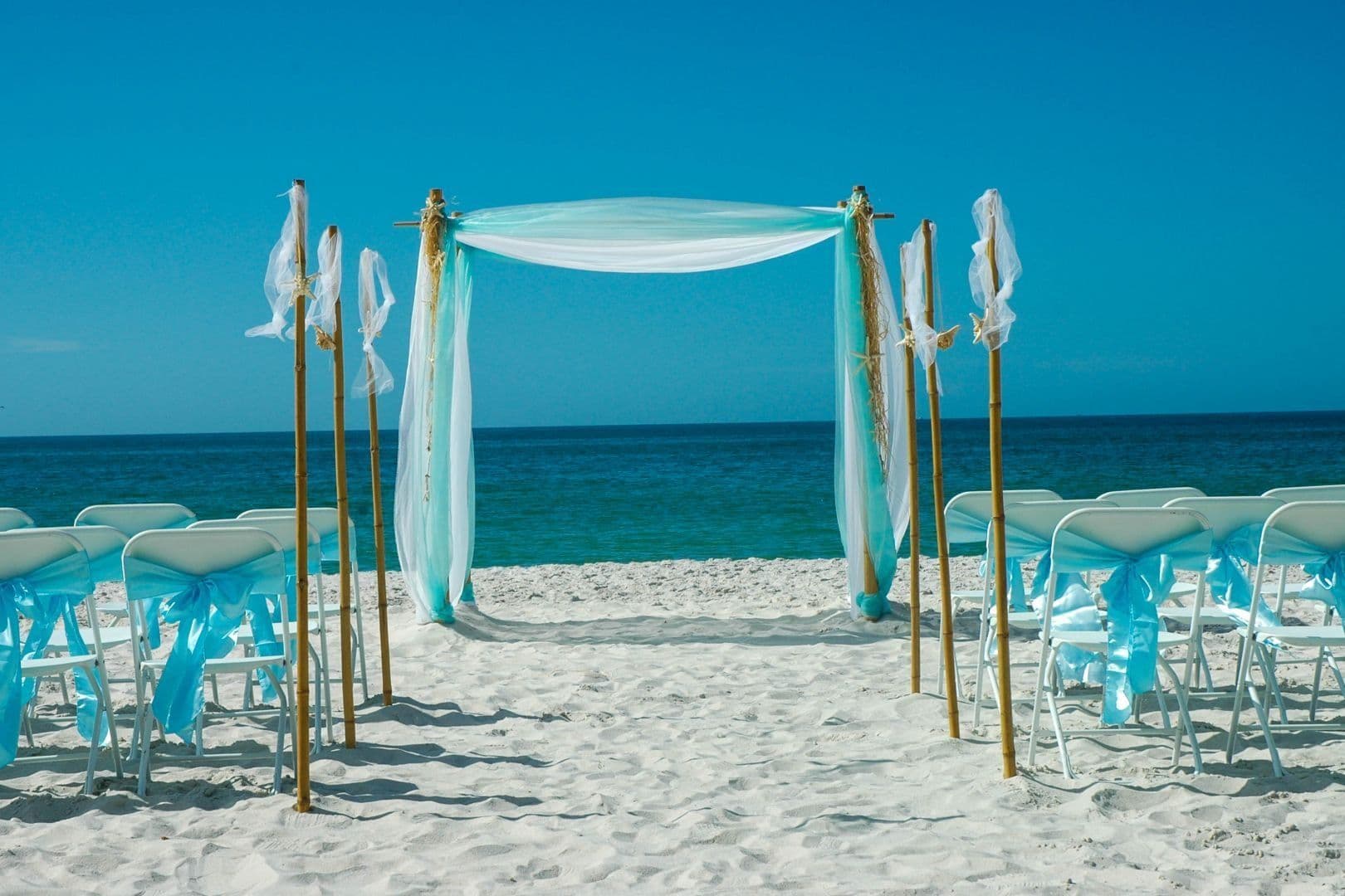 Beach wedding setup with turquoise decorations and ocean view.