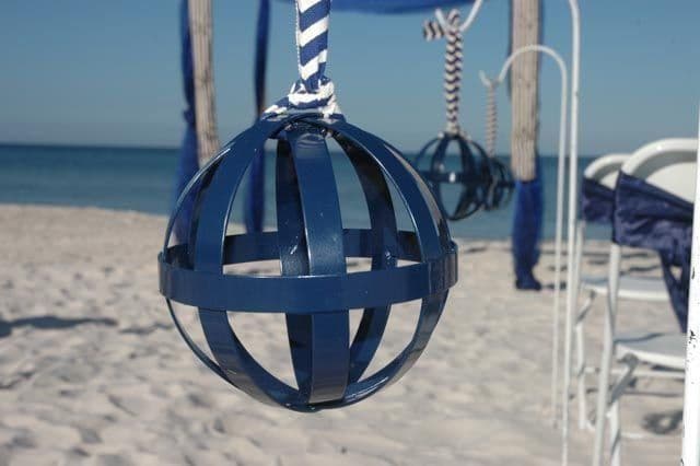 Blue spherical decorative ornaments hanging on a beach with white sand and blue ocean.