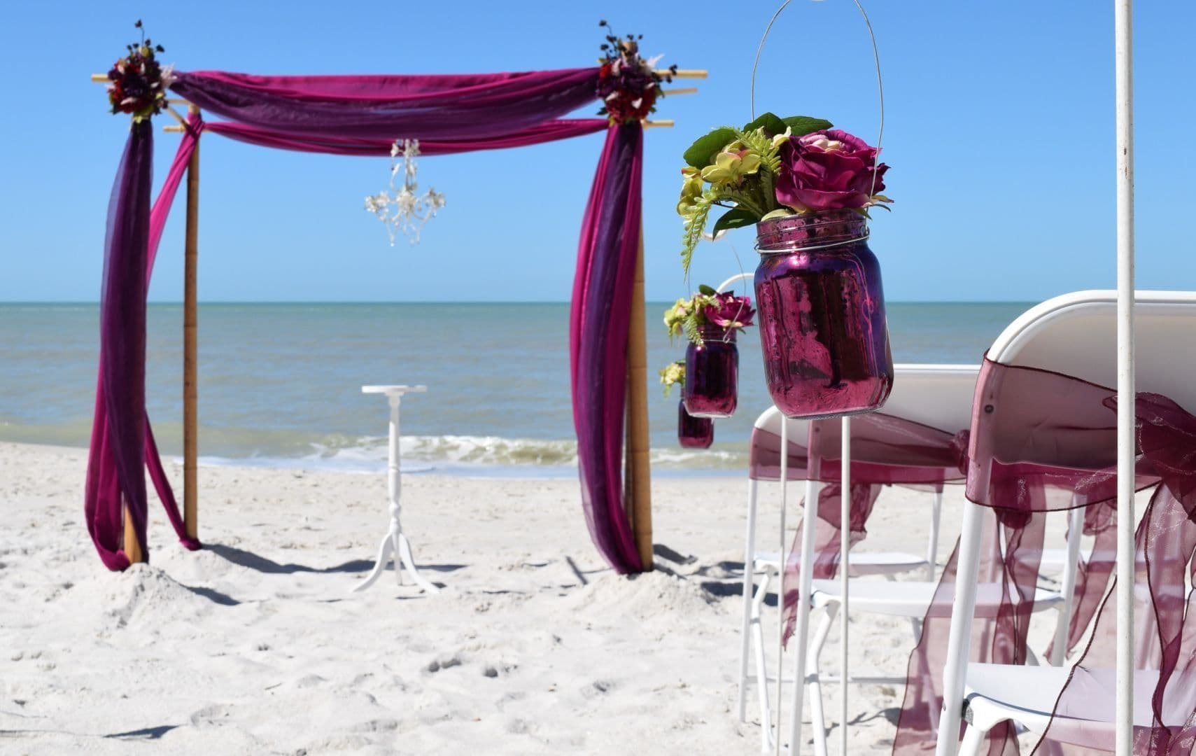 Four-post bamboo canopy with purple draping and floral accents on the beach
