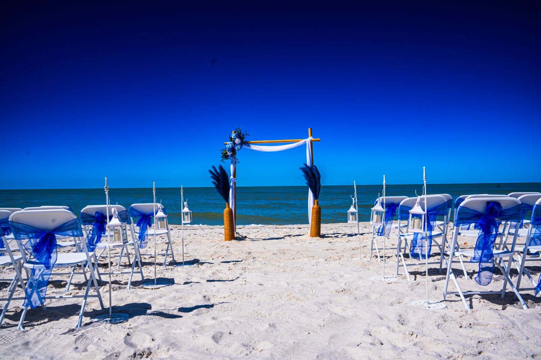 Beach wedding setup: blue and white chairs face an arch with ocean backdrop.