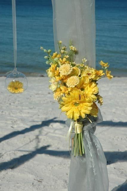 Yellow flower bouquet on a beach with the ocean in the background.