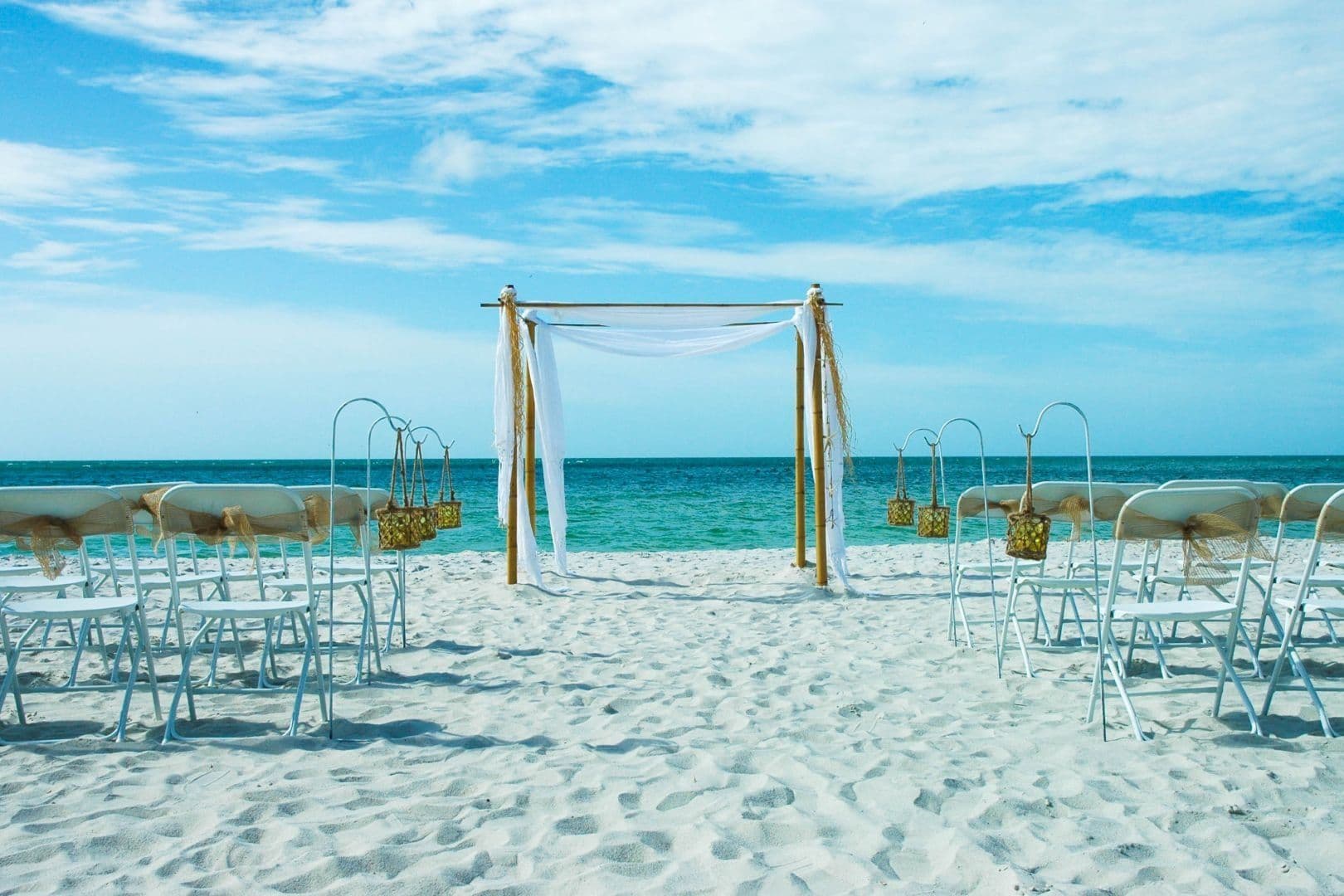 Beach wedding setup with white chairs, arch, and ocean background.