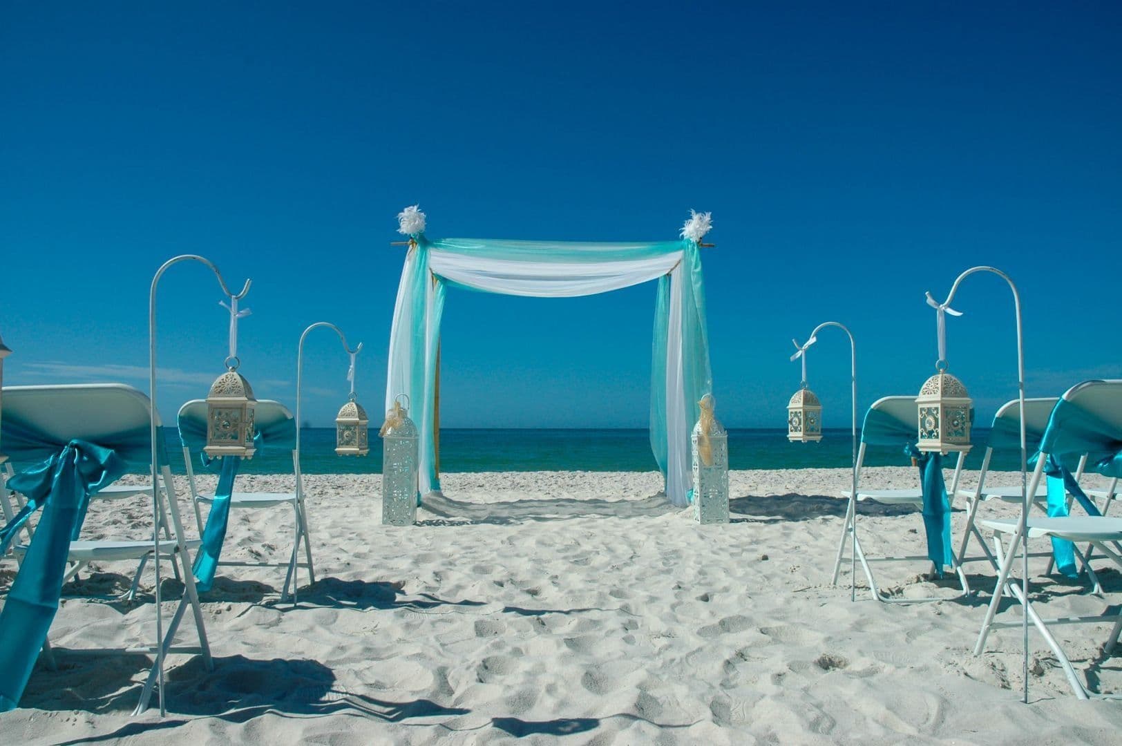 Beach wedding setup: blue and white decorations, ocean view, bright blue sky.