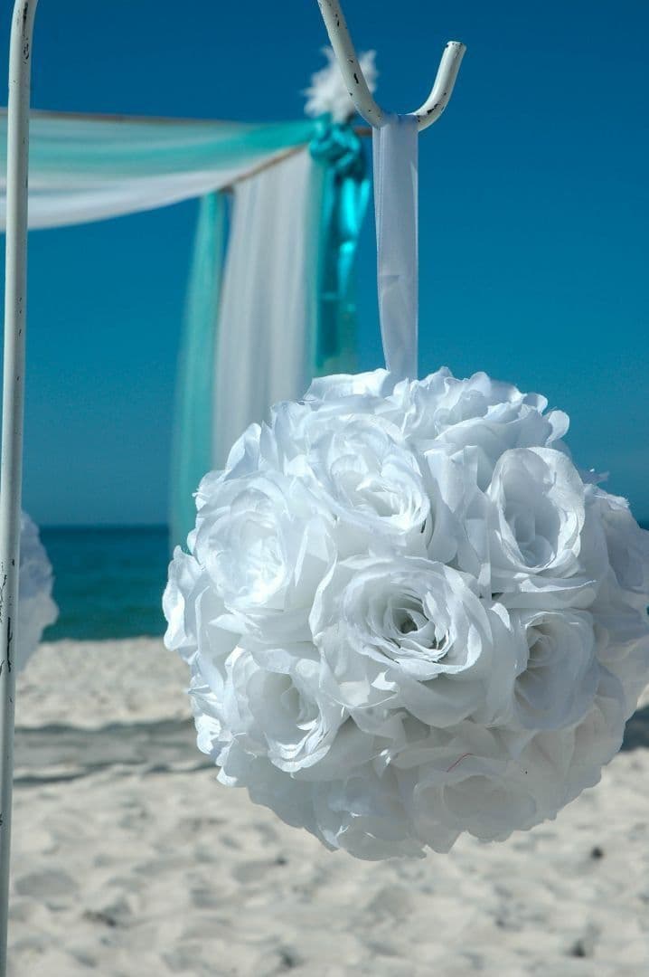 White floral ball decoration hanging on a beach with blue water and sky in the background.