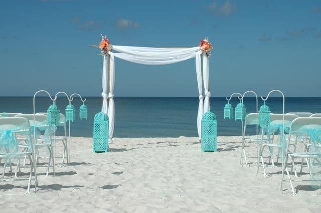 Beach wedding setup with white arch, turquoise accents, and ocean view.