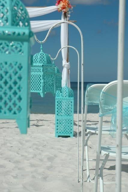 Beach wedding decor with turquoise lanterns and white chairs.