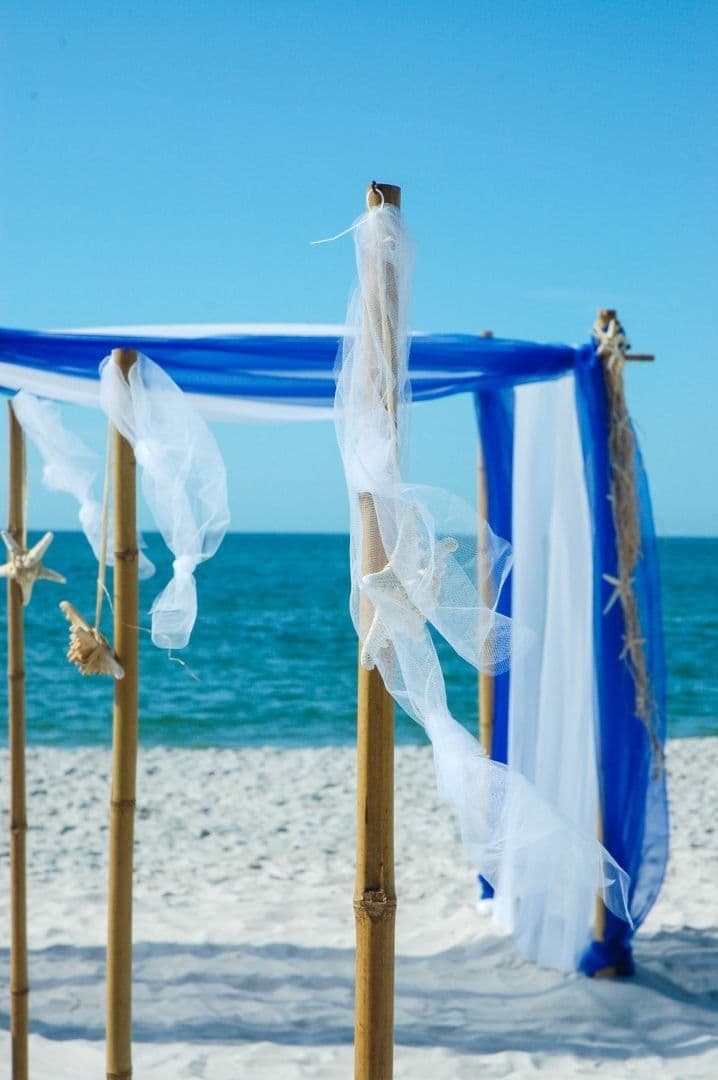 Beach wedding arch with blue and white fabric against a blue sea and sky.