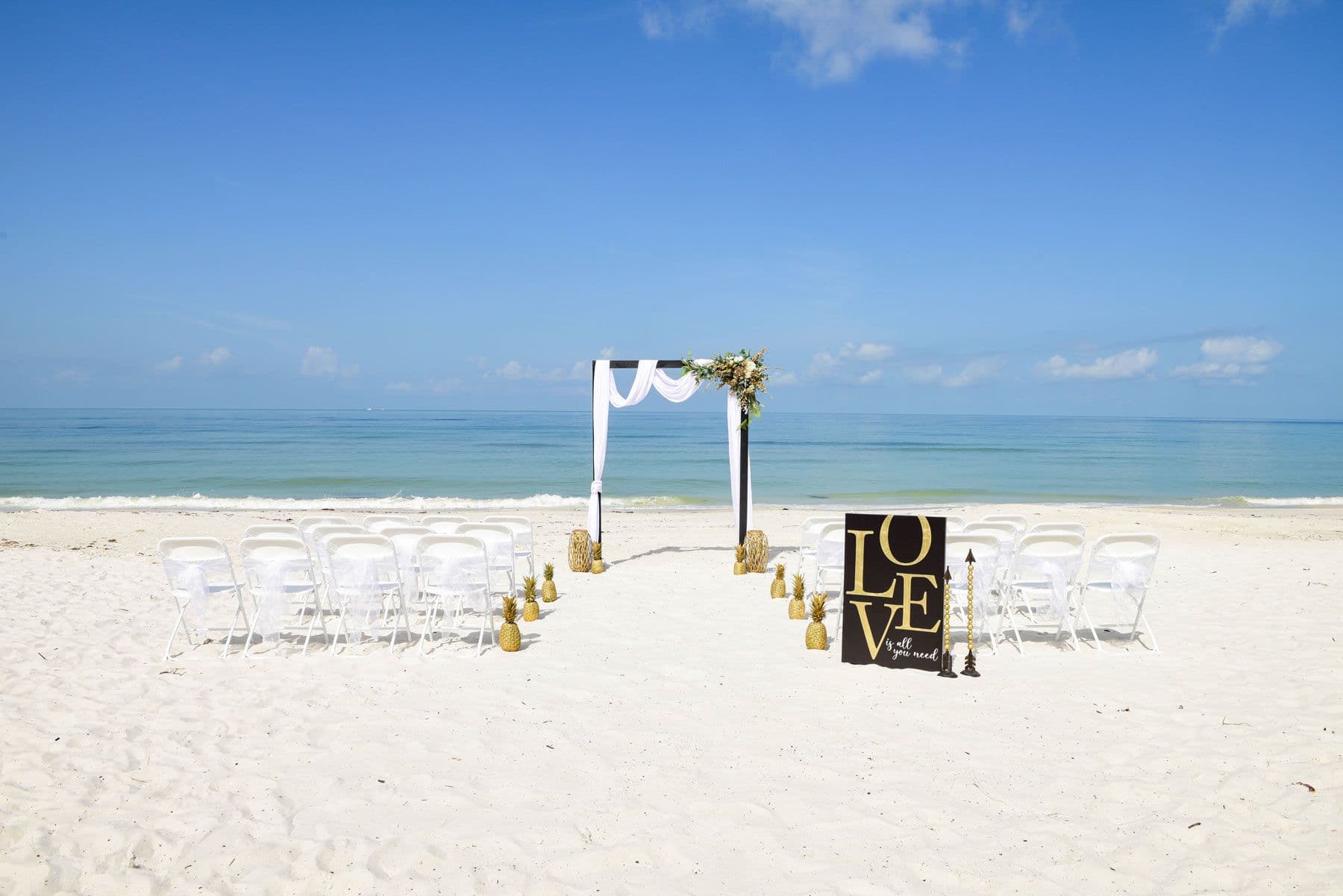 Beach wedding ceremony setup with white chairs, arch, and