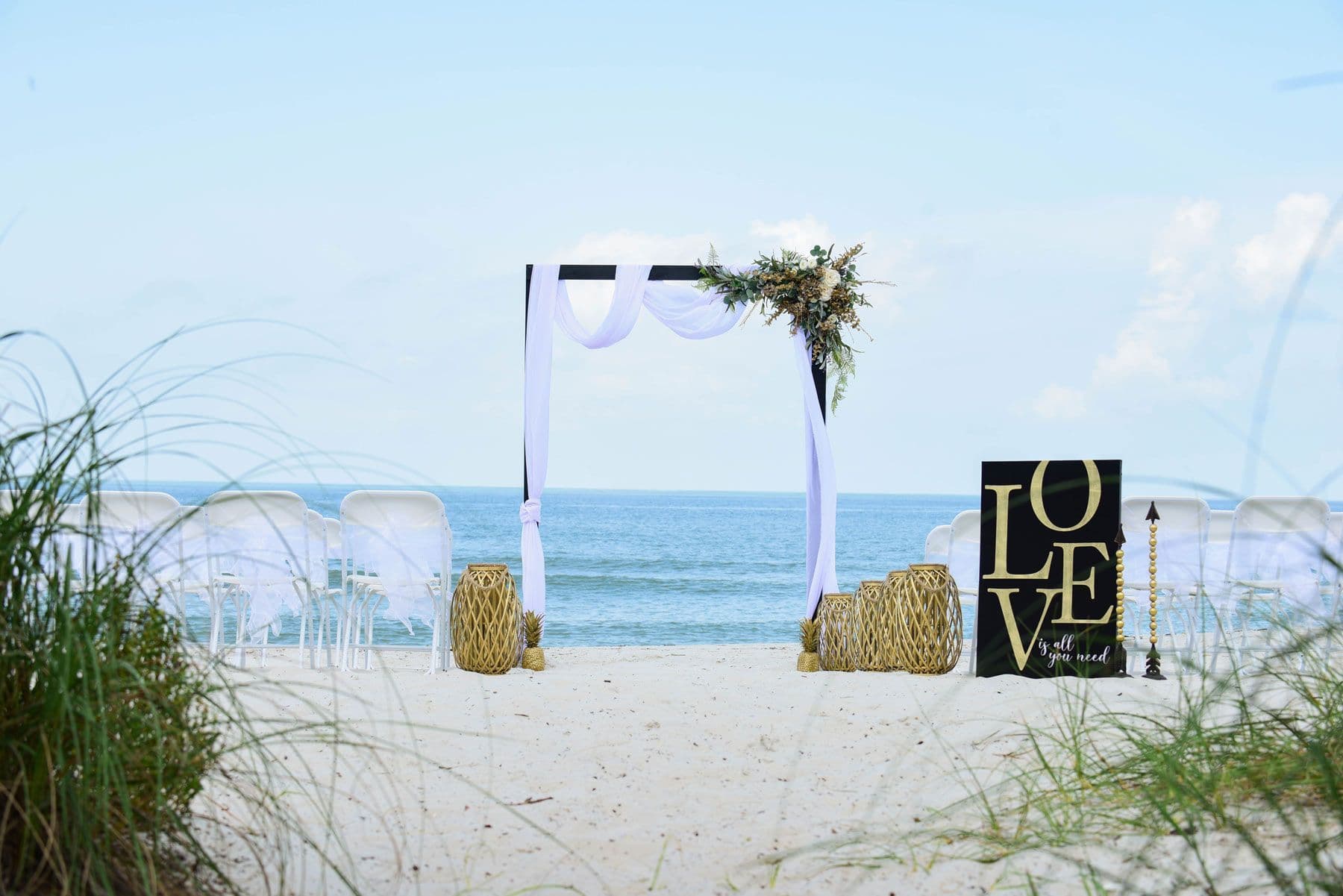 Beach wedding setup with an arch decorated with white fabric and flowers,