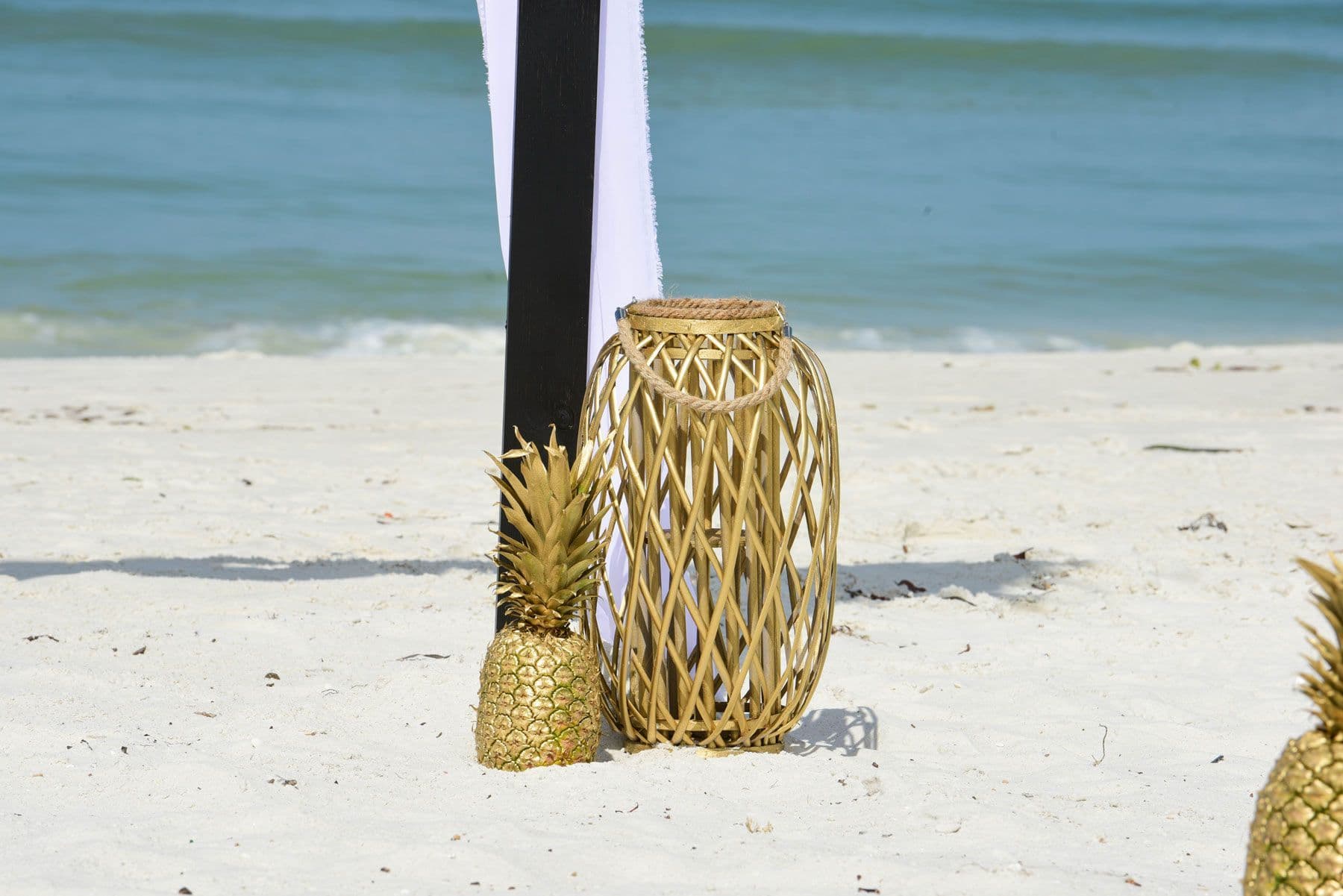 Golden pineapple and lantern on a beach, black and white backdrop, ocean in the background.