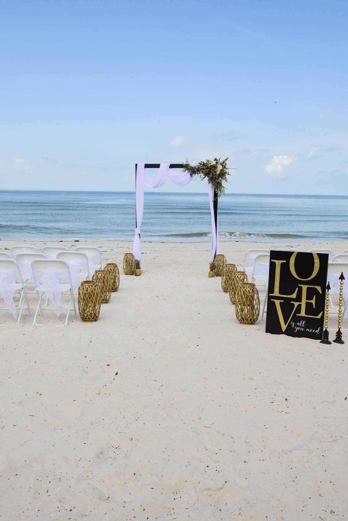 Beach wedding ceremony setup: white chairs, arch,