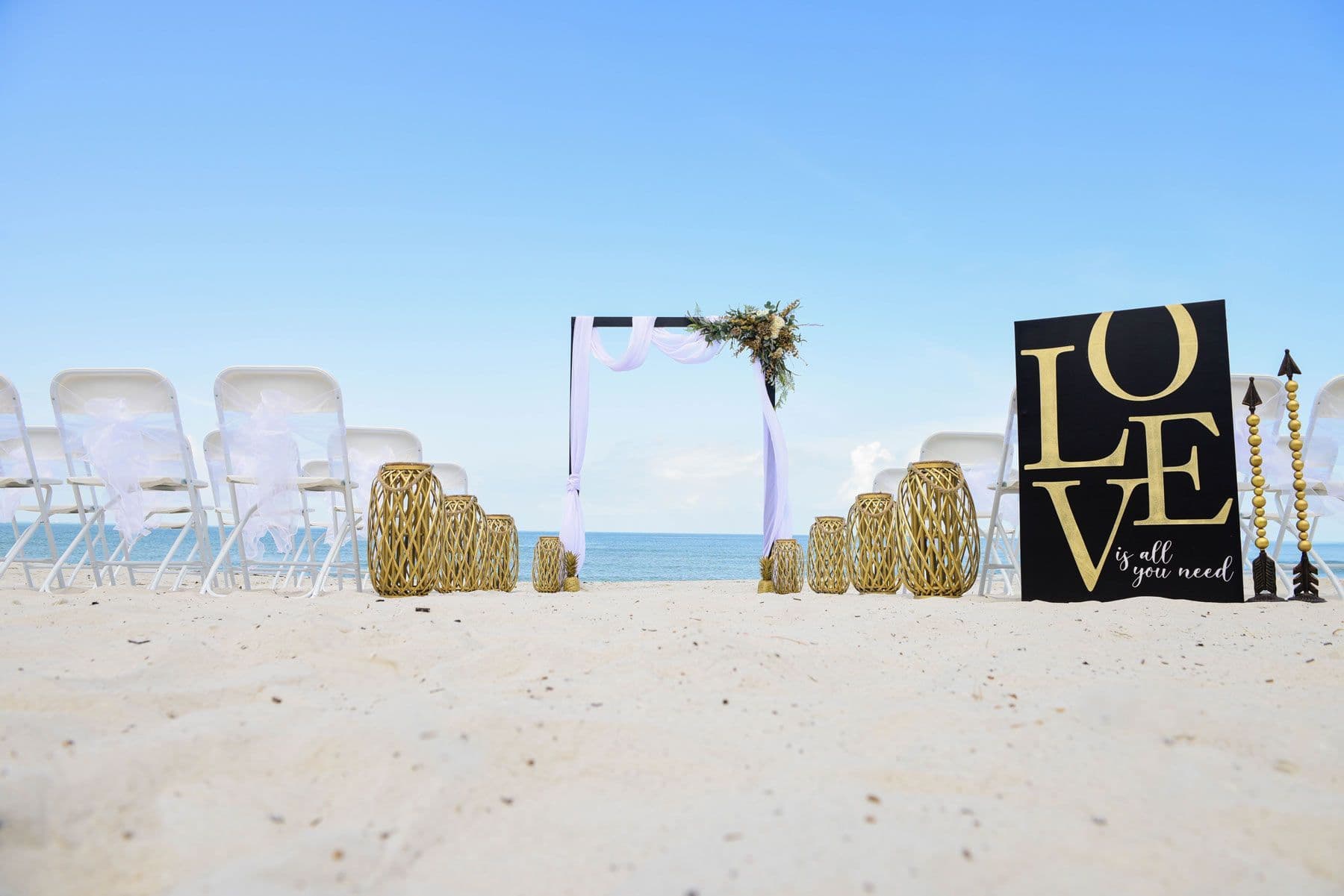 Wedding ceremony setup on a beach: white chairs, arch,