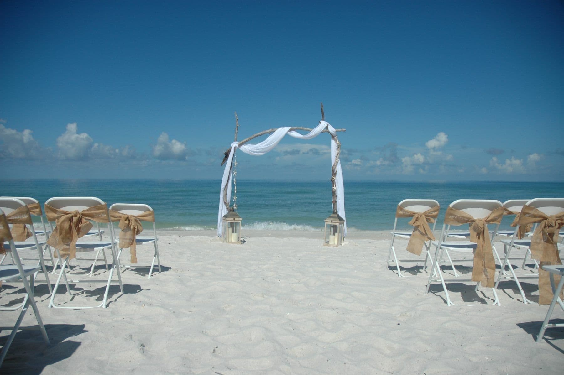 Beach wedding setup with white chairs, arch, and ocean background.