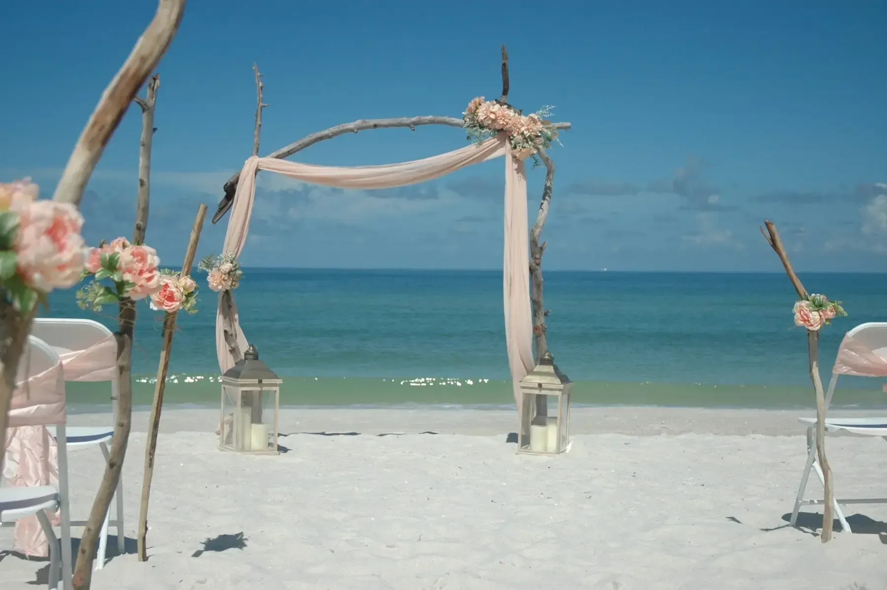 Beach wedding arch decorated with peach flowers and sheer fabric, ocean view.