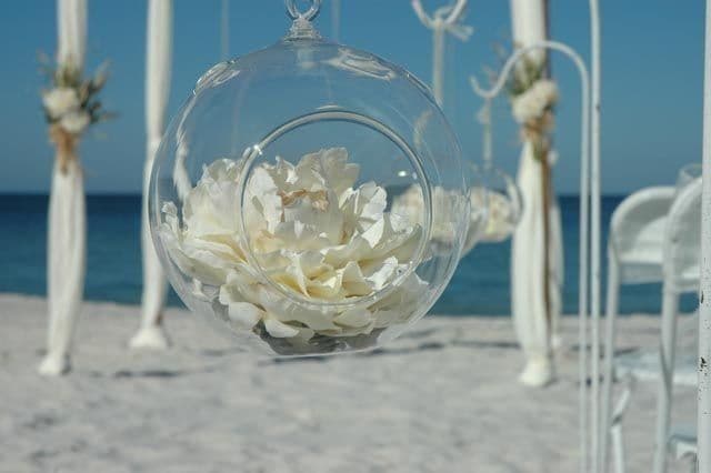 Clear glass orb with white flowers hanging at beach wedding ceremony.