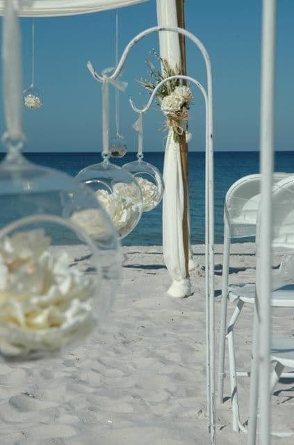 Beach wedding ceremony with white decorations, clear blue sky, ocean backdrop.