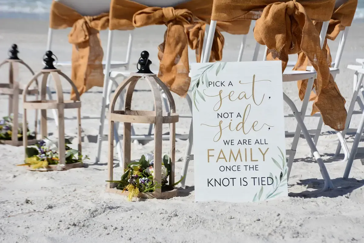Wedding ceremony setup on a beach; sign reads
