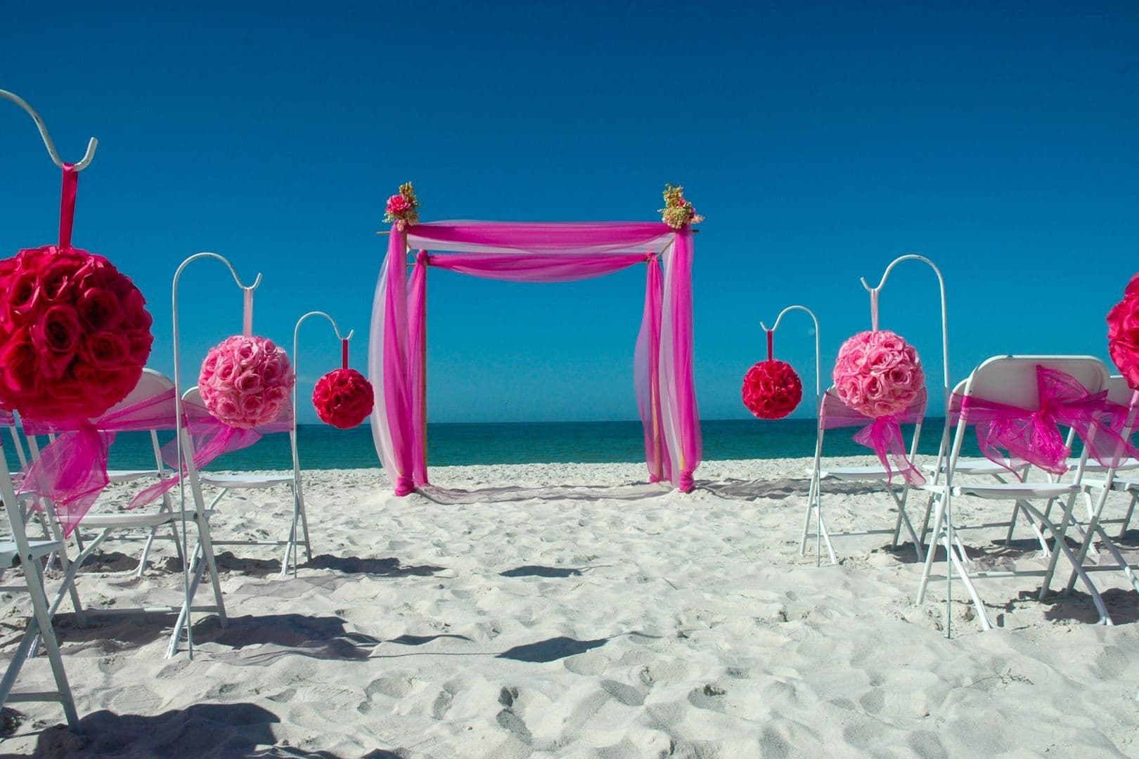 Bamboo canopy with fuchsia pink draping and pink rose pomanders on a Florida beach