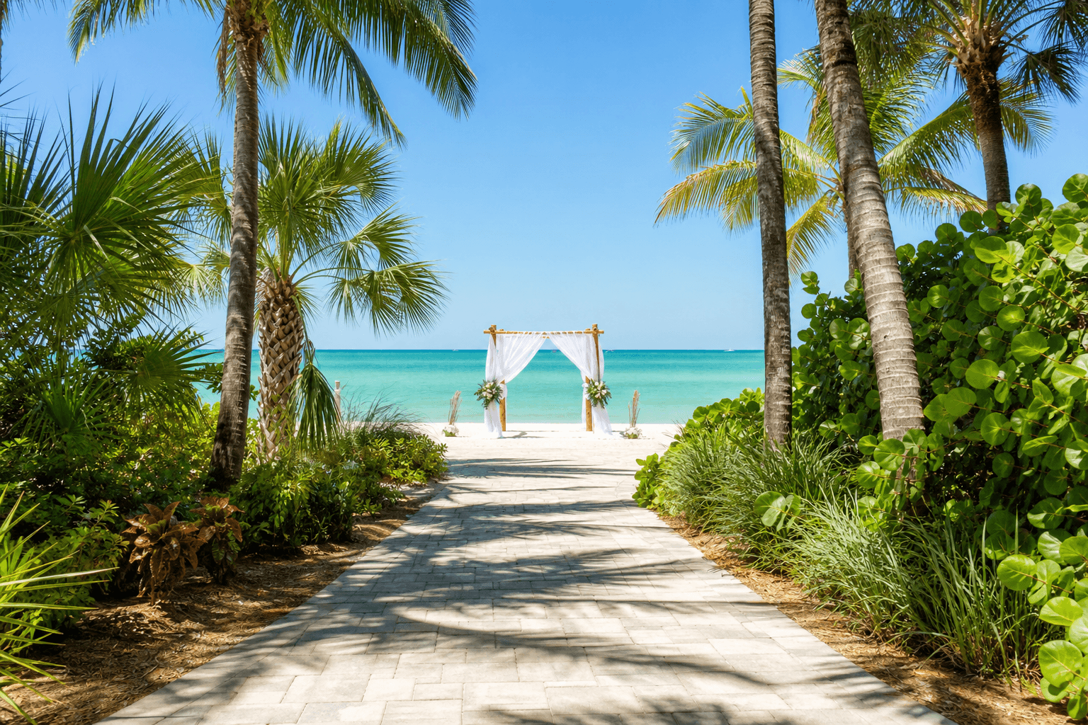 Landscaped beach-access walkway to 8th Ave S Wedding Beach in Naples, Florida, with a wedding arch set up on the sand near the Gulf of Mexico
